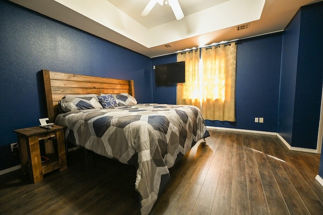 bedroom with baseboards, visible vents, a ceiling fan, wood-type flooring, and a tray ceiling