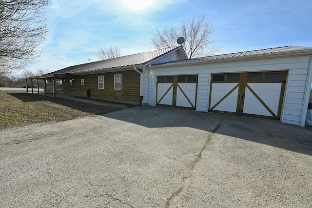 view of side of home featuring aphalt driveway, metal roof, and an attached garage