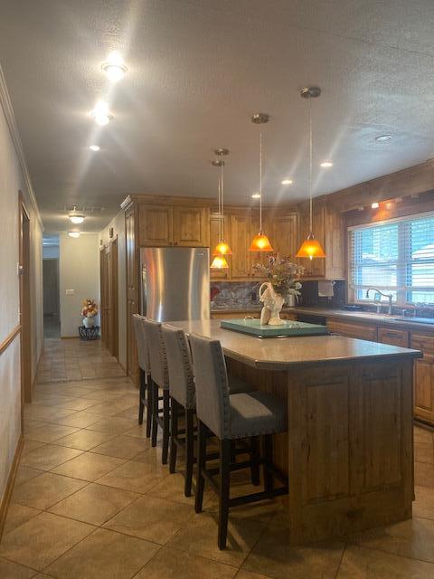 kitchen featuring stainless steel refrigerator, pendant lighting, a kitchen island, sink, and a textured ceiling