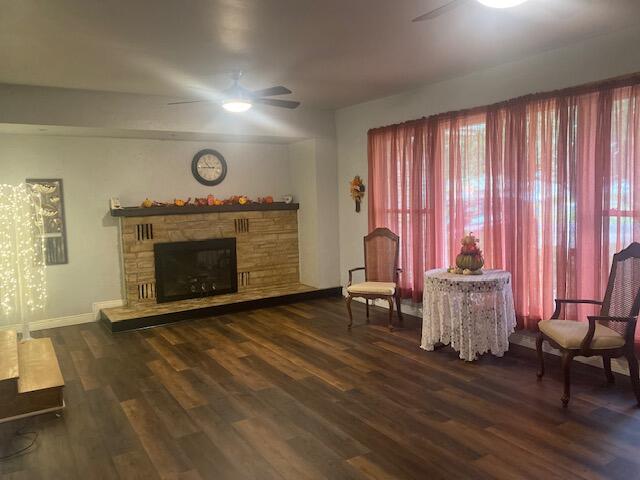 living area with ceiling fan, a stone fireplace, and dark wood-type flooring