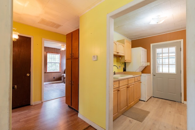 kitchen with light brown cabinets, sink, light hardwood / wood-style floors, stacked washer and clothes dryer, and wood walls