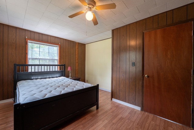 bedroom featuring ceiling fan, wooden walls, and light hardwood / wood-style floors