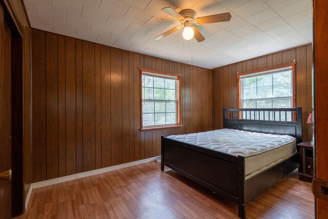 bedroom with wood walls, wood-type flooring, multiple windows, and ceiling fan