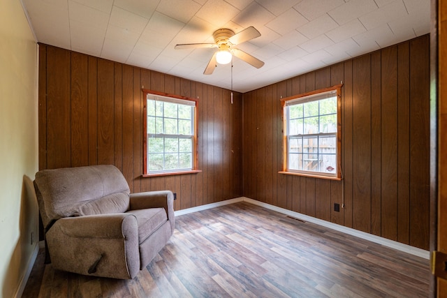 living area with ceiling fan, wooden walls, a wealth of natural light, and wood-type flooring