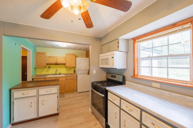 kitchen with light wood-type flooring, ceiling fan, stacked washer / dryer, sink, and stainless steel gas stove