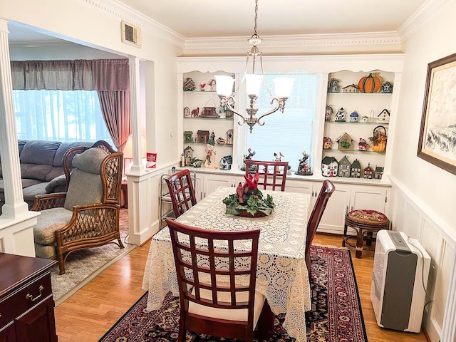 dining room featuring a wainscoted wall, ornamental molding, a decorative wall, light wood-style flooring, and a notable chandelier
