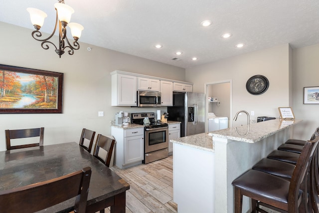 kitchen with separate washer and dryer, decorative light fixtures, stainless steel appliances, light stone countertops, and white cabinets