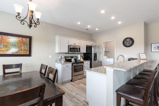 kitchen with a kitchen breakfast bar, appliances with stainless steel finishes, white cabinets, a notable chandelier, and independent washer and dryer
