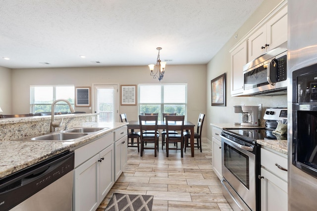 kitchen featuring an inviting chandelier, a sink, decorative light fixtures, appliances with stainless steel finishes, and white cabinetry
