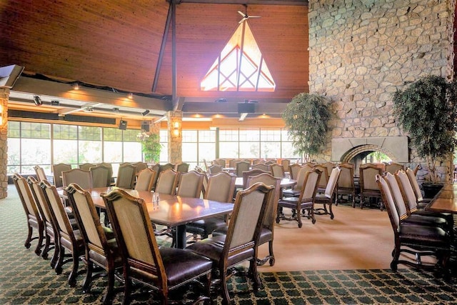 carpeted dining area featuring a stone fireplace, wood ceiling, and a high ceiling