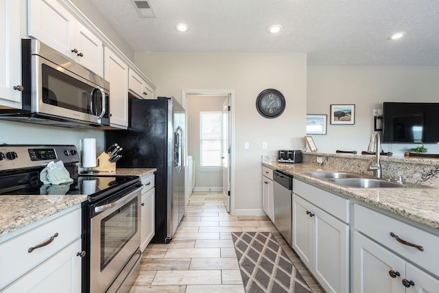 kitchen featuring sink, light stone countertops, white cabinets, appliances with stainless steel finishes, and a textured ceiling