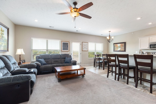 carpeted living room with ceiling fan with notable chandelier and a textured ceiling