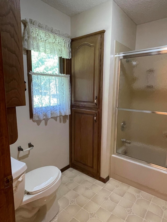 bathroom with shower / bath combination with glass door, a textured ceiling, toilet, and tile patterned floors