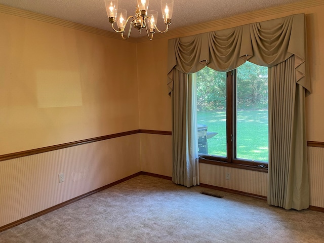 carpeted empty room featuring a textured ceiling, crown molding, and a notable chandelier