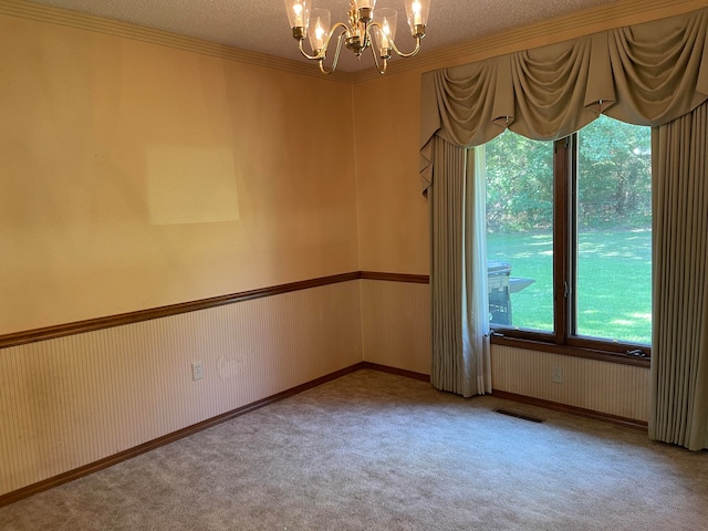 carpeted spare room with a textured ceiling, crown molding, and a chandelier