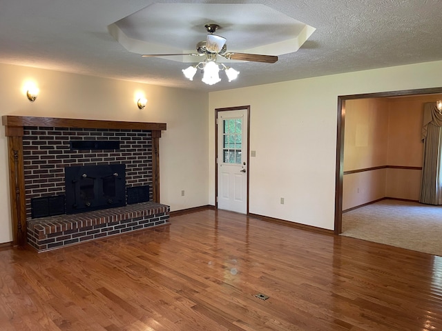 unfurnished living room featuring a brick fireplace, ceiling fan, wood-type flooring, and a textured ceiling