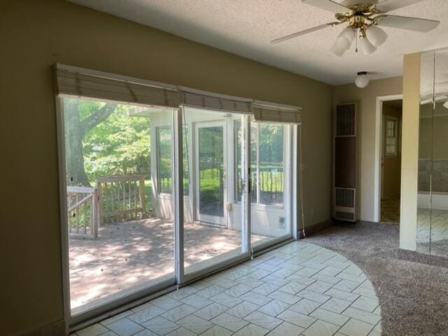 doorway to outside featuring light colored carpet, a textured ceiling, and ceiling fan