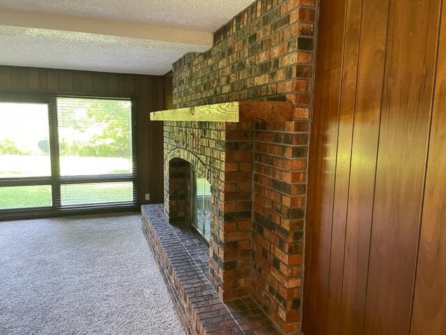 carpeted living room featuring a fireplace, beam ceiling, wood walls, and a textured ceiling