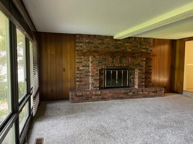 unfurnished living room featuring carpet floors, wood walls, a fireplace, and a wealth of natural light