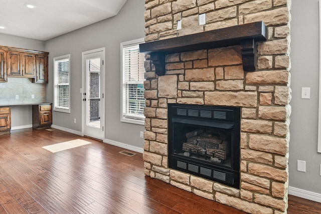 room details featuring hardwood / wood-style flooring, built in desk, a stone fireplace, and backsplash