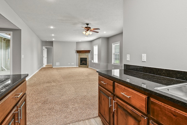 kitchen featuring ceiling fan, light carpet, sink, dark stone countertops, and a fireplace