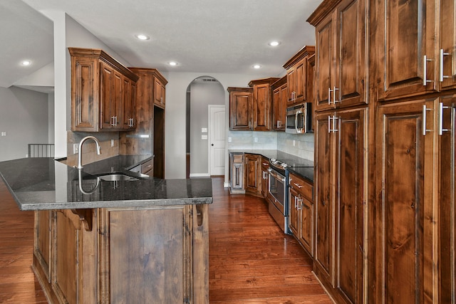 kitchen with appliances with stainless steel finishes, dark hardwood / wood-style floors, dark stone counters, and decorative backsplash