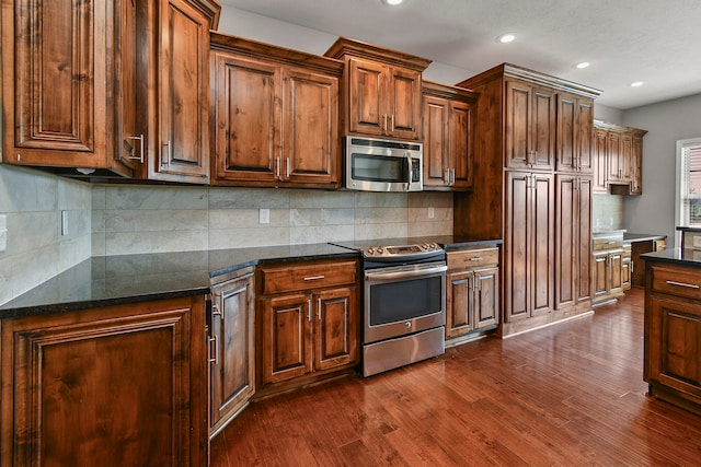 kitchen featuring stainless steel appliances, backsplash, dark hardwood / wood-style flooring, and dark stone countertops