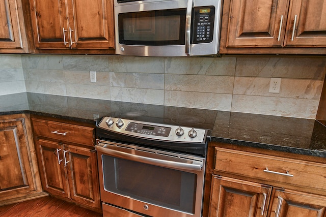 kitchen with dark stone countertops, backsplash, stainless steel appliances, and dark hardwood / wood-style flooring