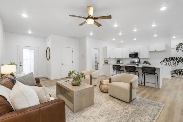 living room featuring baseboards, light wood finished floors, a ceiling fan, and recessed lighting