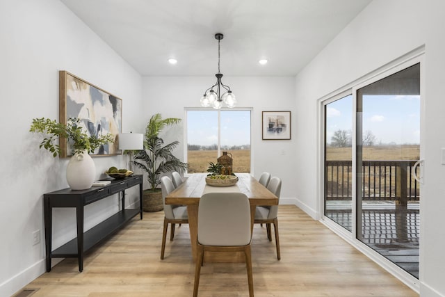 dining area with light wood-type flooring, baseboards, and an inviting chandelier