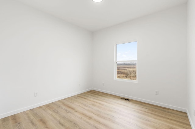 spare room featuring light wood finished floors, visible vents, and baseboards