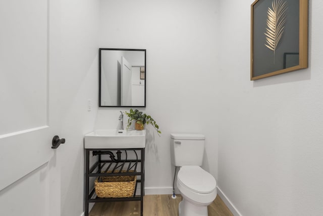 half bathroom with baseboards, a sink, toilet, and wood finished floors