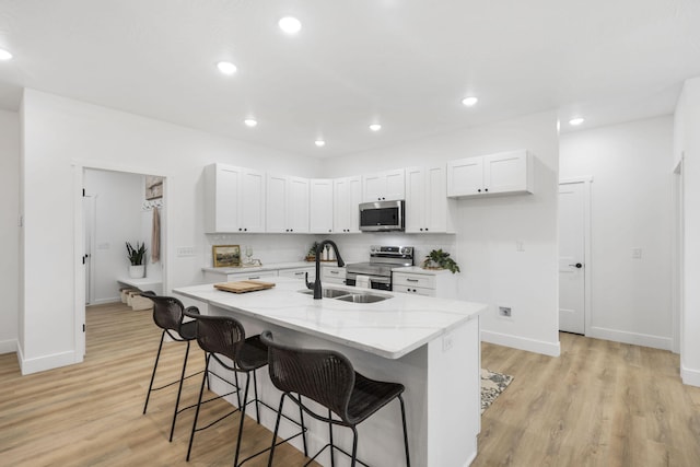 kitchen featuring stainless steel appliances, a sink, light wood-style floors, light stone countertops, and a kitchen bar