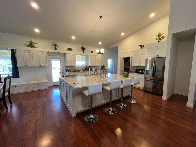 kitchen with dark wood-type flooring, decorative light fixtures, a large island with sink, stainless steel refrigerator with ice dispenser, and white cabinetry