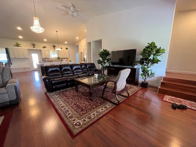 living room with ceiling fan with notable chandelier, high vaulted ceiling, and dark wood-type flooring