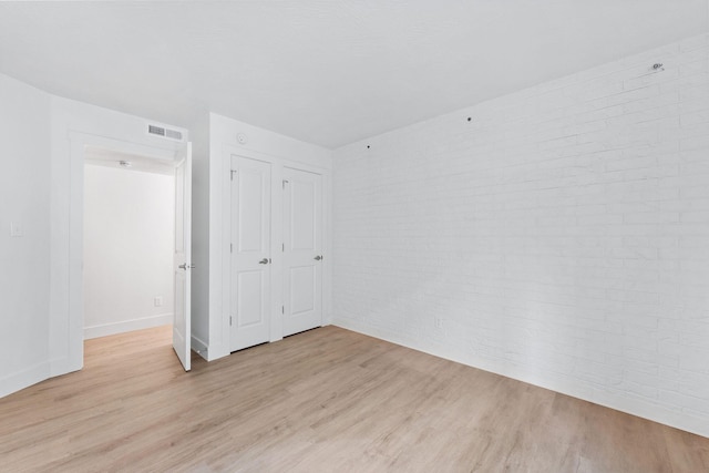unfurnished bedroom with light wood-style flooring, visible vents, baseboards, and brick wall