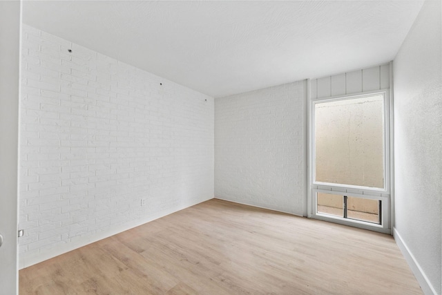 spare room featuring brick wall and wood finished floors