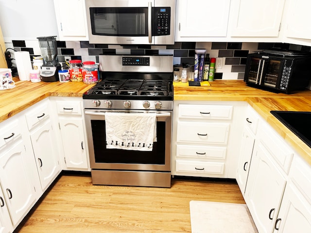 kitchen with white cabinets, light hardwood / wood-style flooring, backsplash, stainless steel appliances, and wood counters