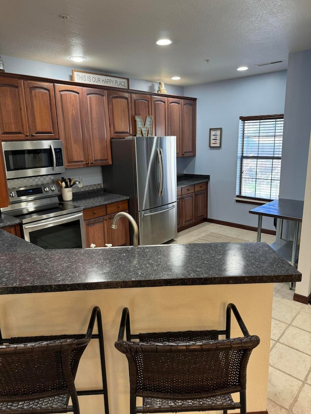 kitchen featuring sink, light tile patterned floors, appliances with stainless steel finishes, kitchen peninsula, and a breakfast bar area