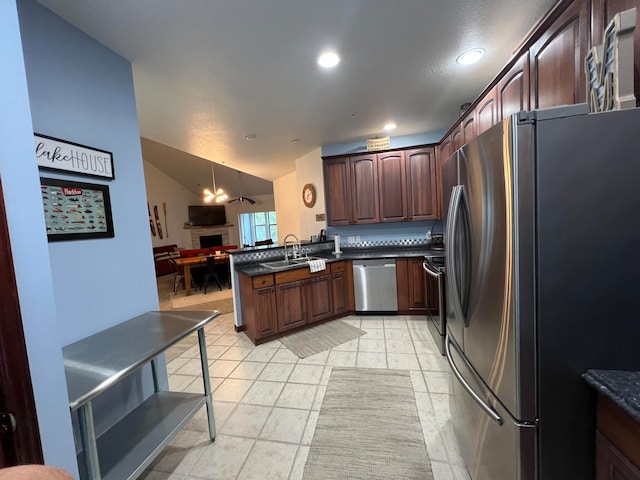 kitchen with pendant lighting, sink, vaulted ceiling, appliances with stainless steel finishes, and kitchen peninsula