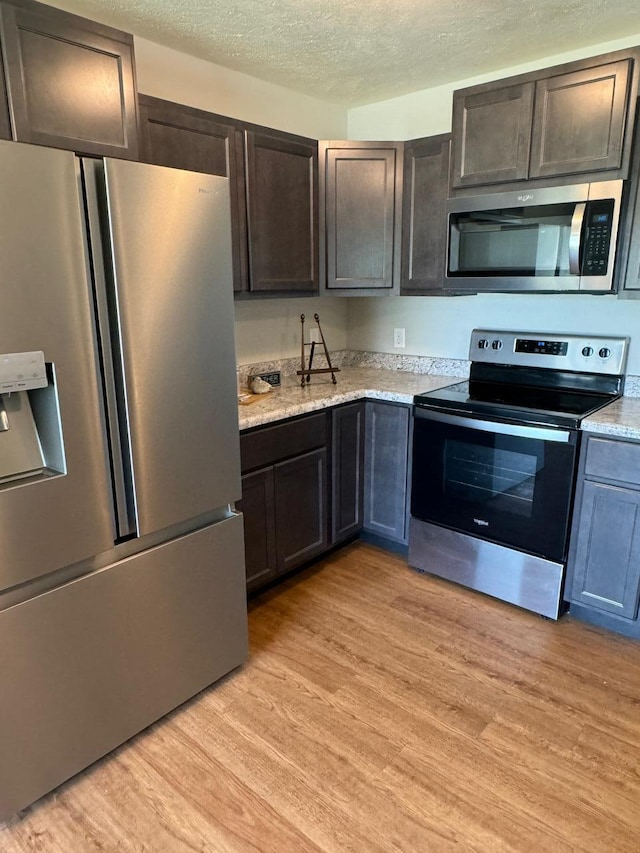 kitchen with stainless steel appliances, dark brown cabinetry, a textured ceiling, and light wood-type flooring