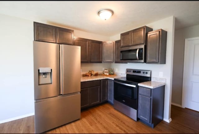 kitchen with appliances with stainless steel finishes, dark brown cabinets, and light hardwood / wood-style floors