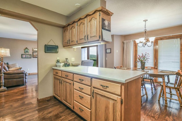 kitchen featuring dark wood finished floors, a peninsula, light countertops, and an inviting chandelier