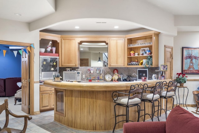 kitchen featuring kitchen peninsula, decorative backsplash, light brown cabinets, and a breakfast bar