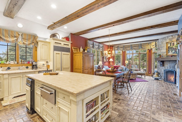 kitchen with tile countertops, beamed ceiling, a fireplace, and a wealth of natural light