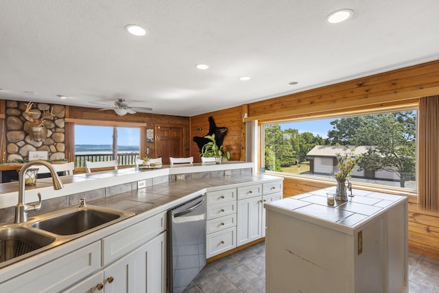 kitchen featuring tile countertops, wood walls, white cabinets, and stainless steel dishwasher