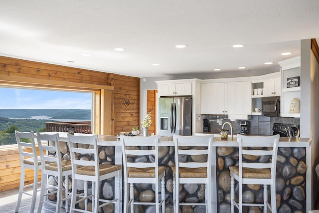 kitchen featuring wood walls, white cabinets, appliances with stainless steel finishes, and a kitchen breakfast bar