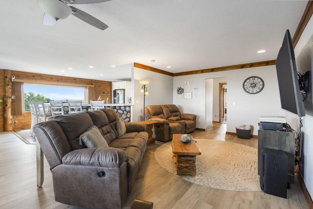 living room with ceiling fan, light hardwood / wood-style flooring, wooden walls, ornamental molding, and a textured ceiling