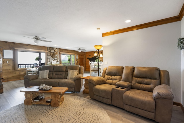 living room with ceiling fan, light hardwood / wood-style flooring, ornamental molding, wood walls, and a textured ceiling