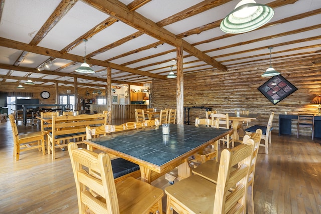 dining space with hardwood / wood-style floors, rustic walls, and beam ceiling